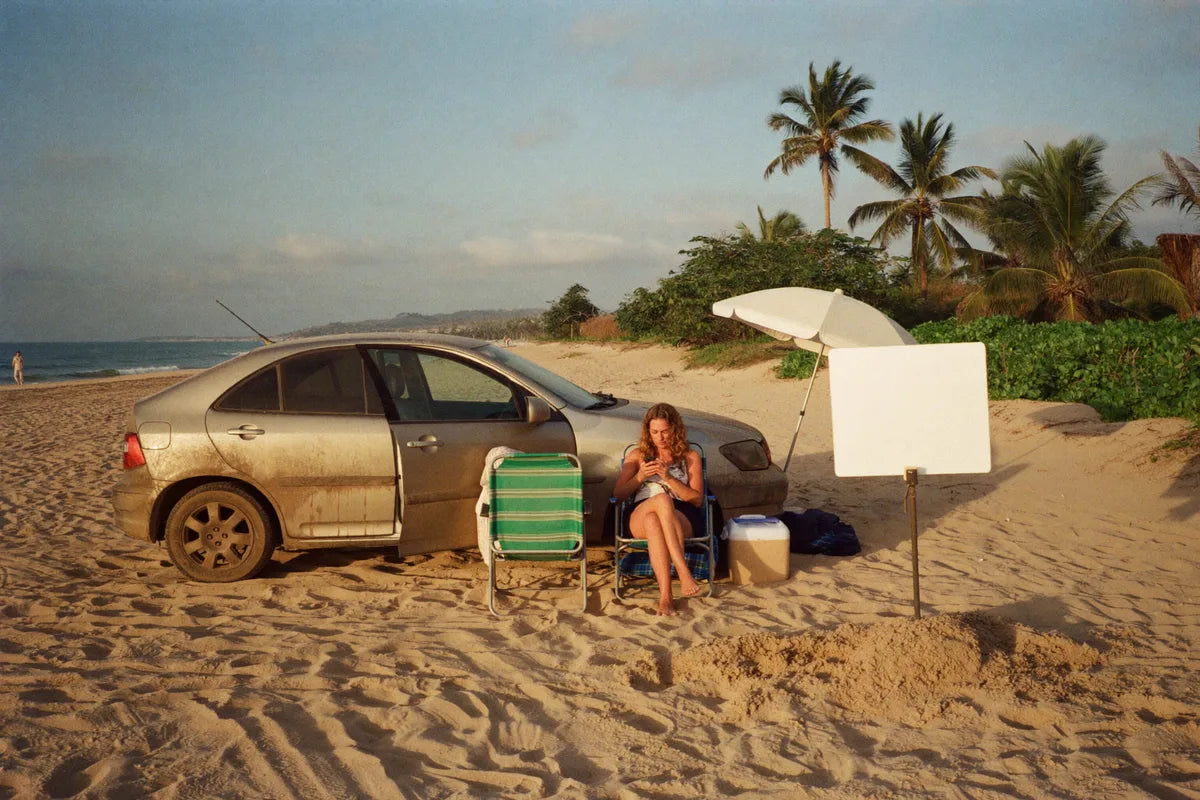 Carro parado na areia da praia com cadeira, isopor e guarda-sol
